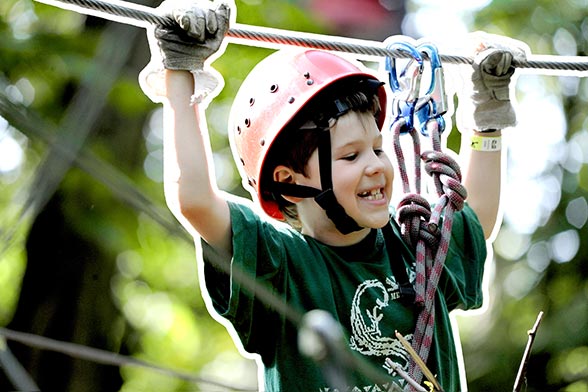 Ein Junge mit Helm gesichert an einem Stahlseil klettert im Hochseilgarten tree2tree